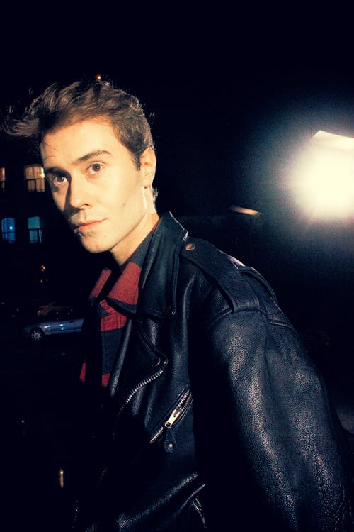 Photo of a Young Man in a Leather Jacket Walking Outside in the Dark 