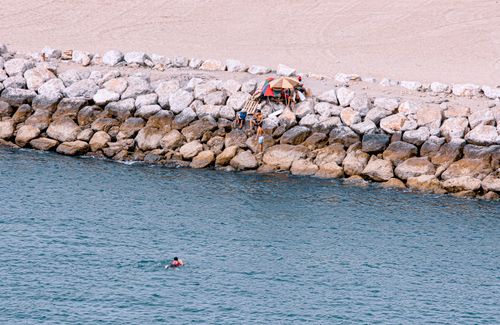 Free Aerial view of people relaxing on rocky beach with turquoise water. Stock Photo