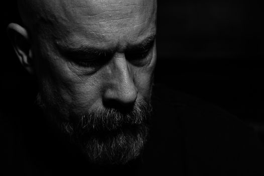 Dramatic black and white portrait photo of a contemplative man with a beard.