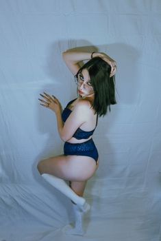 Artistic fashion portrait of a woman posing in blue lingerie and white socks against a white background.