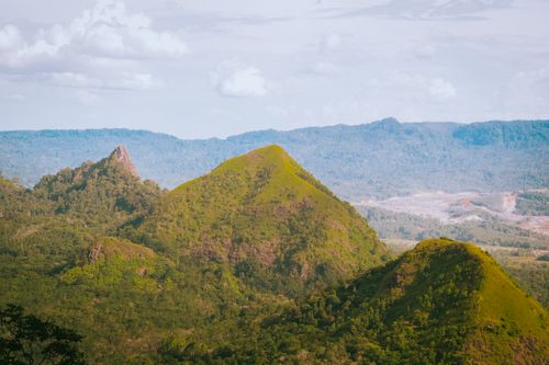 Free Breathtaking view of lush green hills and mountains under cloudy blue sky. Stock Photo