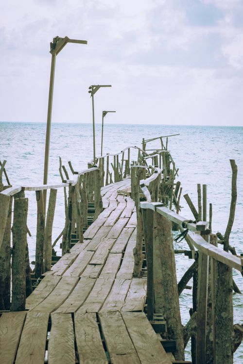 Free A rustic wooden pier stretches into calm sea at Sungai Liat, Indonesia, under cloudy skies. Stock Photo