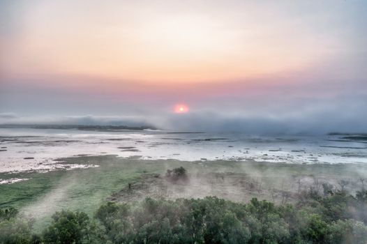 A tranquil sunrise view over Weaver's foggy wetlands with mist rolling over the landscape.