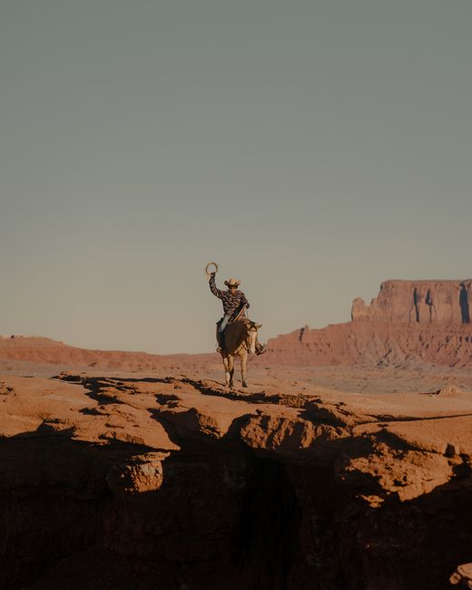 A cowboy on horseback silhouetted against the sandstone cliffs of Monument Valley, Arizona.