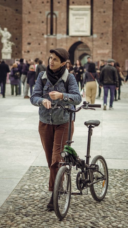 Free Casually dressed woman walks her bike through a historic city square on a cool day. Stock Photo