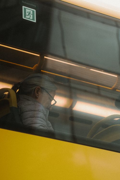 Free A senior woman commuting on a Berlin bus captured through a window reflection. Stock Photo