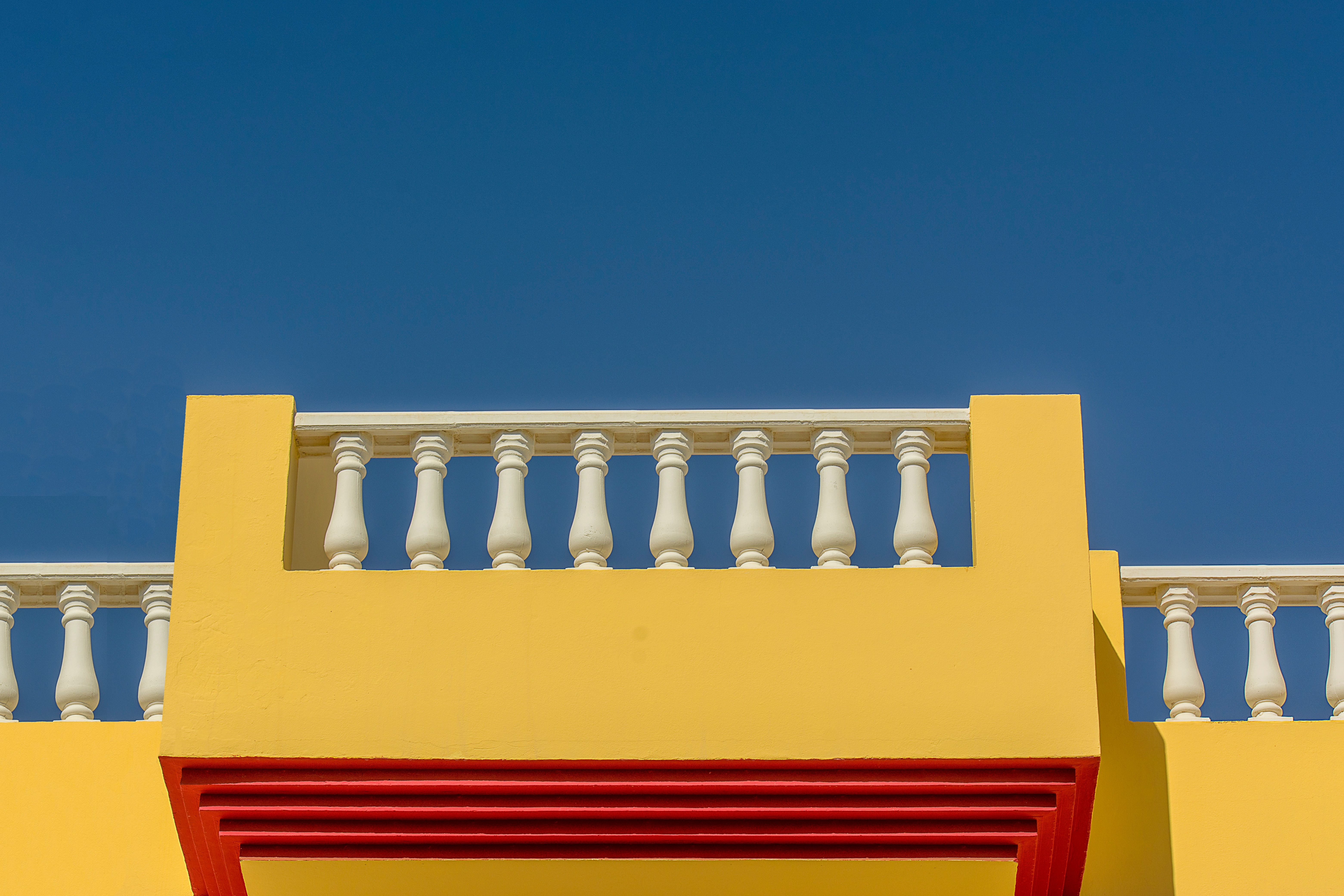 Vibrant yellow balcony with white balustrades against a clear blue sky.