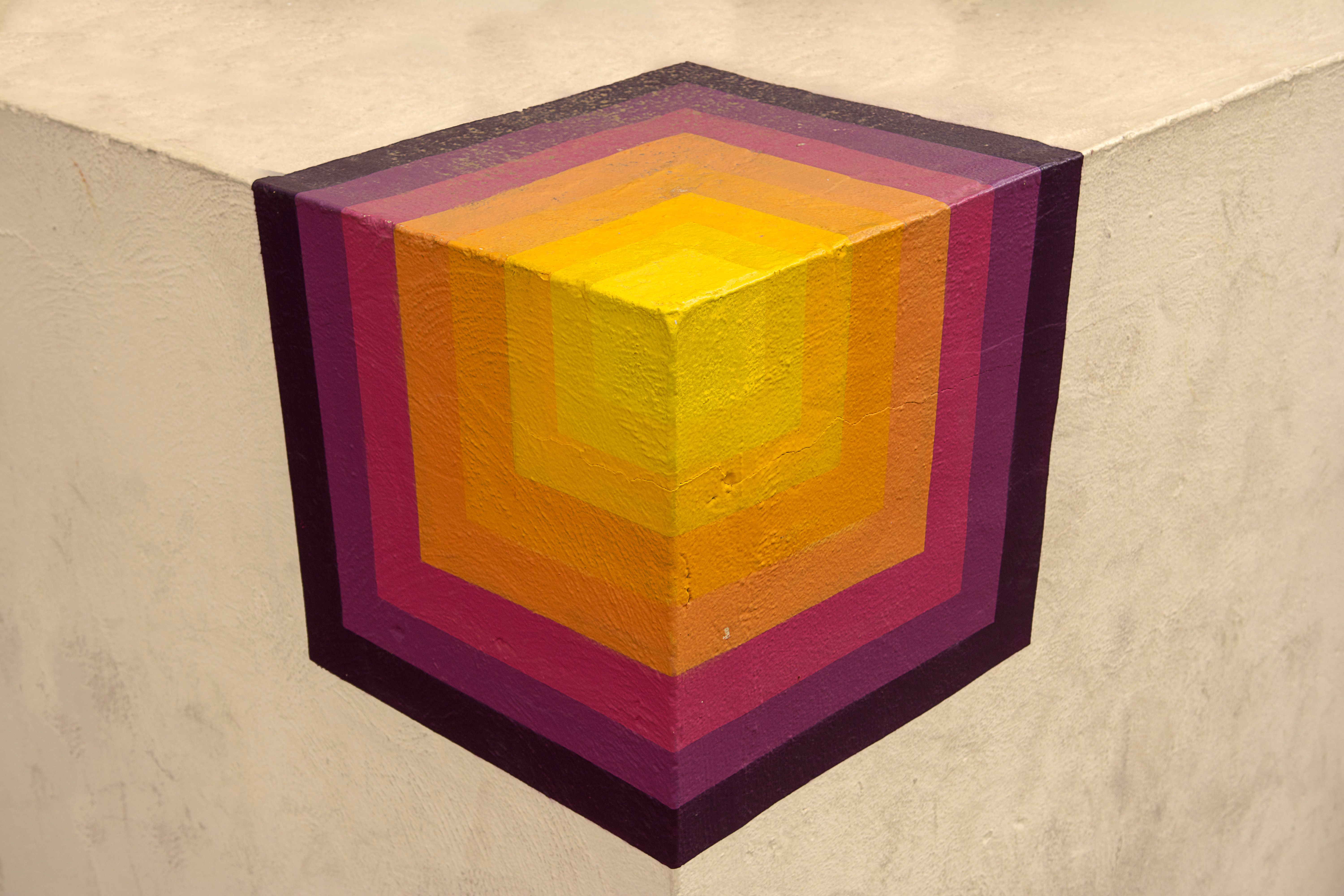 Vibrant geometric mural painted on a concrete wall corner, featuring layered colorful cubes.