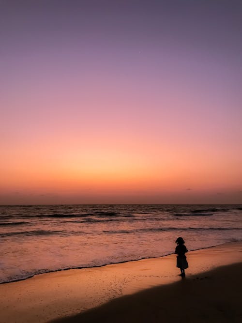 Silhouette of Woman Standing on Sea Shore at Sunset