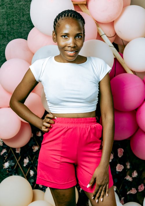 Free Smiling woman in a white top and red shorts posing with pink balloons, exuding happiness and style. Stock Photo