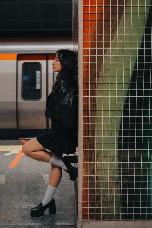 Free Stylish woman in black attire posing against a tiled wall in an urban subway station. Stock Photo