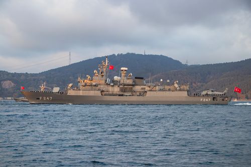 Free Turkish warship F247 cruising through calm waters with a scenic mountainous backdrop. Stock Photo