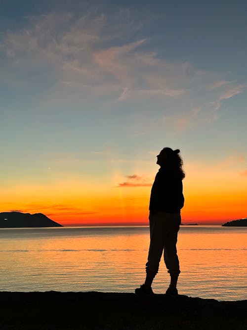 Silhouette of a Tourist on the Ocean Shore with the Evening Sky in the Background