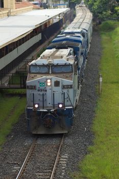 A cargo train travels through an industrial area on a sunny day, showcasing railway logistics.
