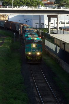 Cargo train on railway tracks passing through an urban area under a bridge.