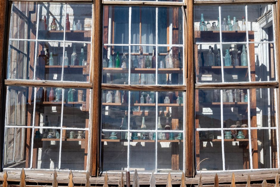 A collection of vintage glass bottles displayed on wooden shelves behind a window.