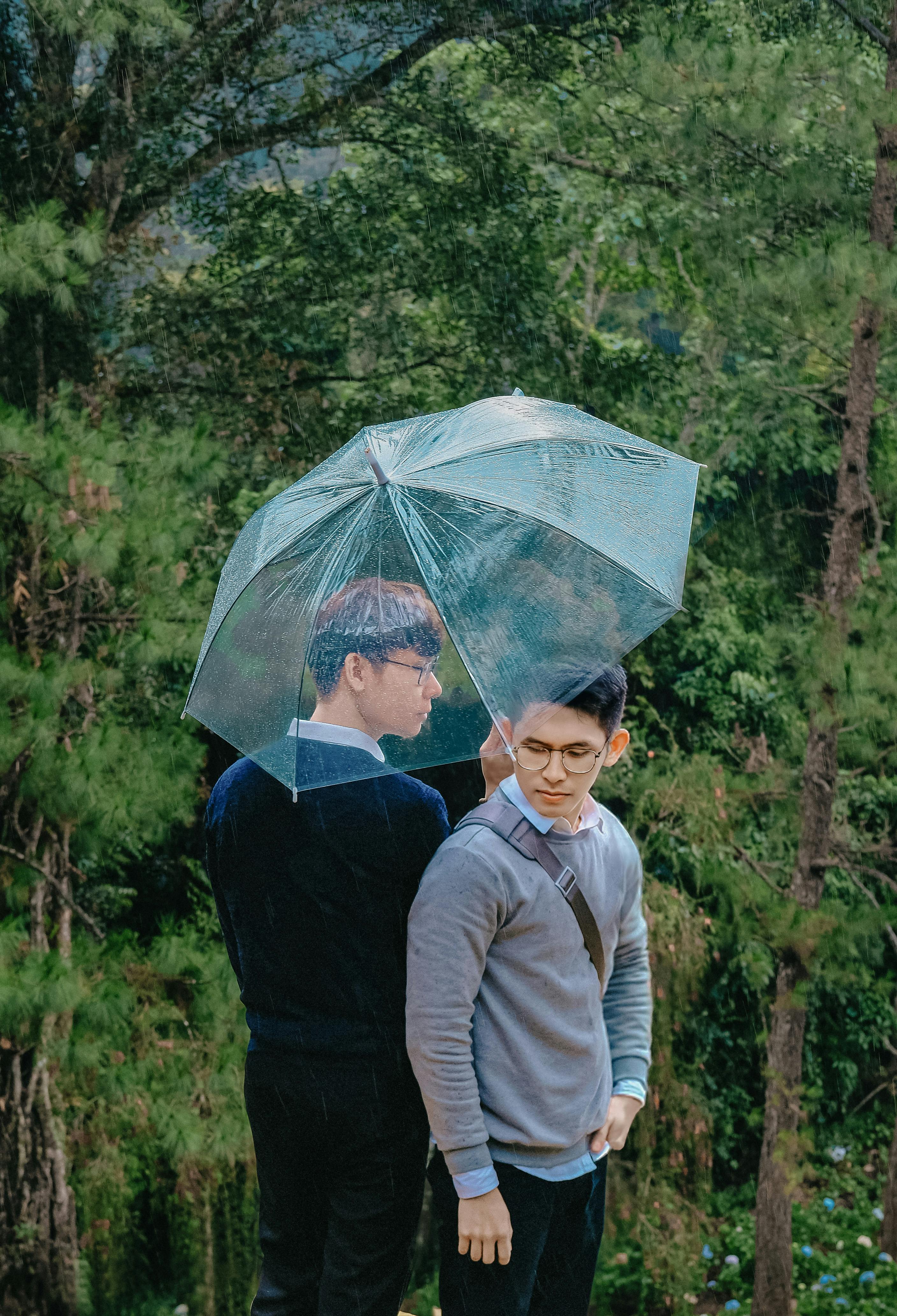 Two teenagers sharing an umbrella in a lush forest, capturing a summer moment.
