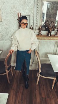 Stylish woman in turtleneck and denim skirt in a chic cafe interior.
