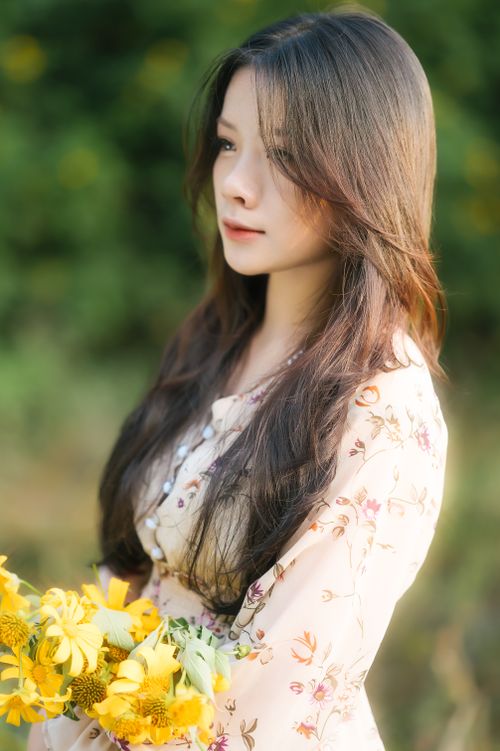 Free Young woman in floral dress holding yellow flowers in a serene outdoor setting. Stock Photo