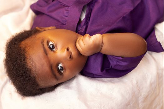 Close-up of a baby in a purple outfit lying down, showcasing innocence and curiosity.
