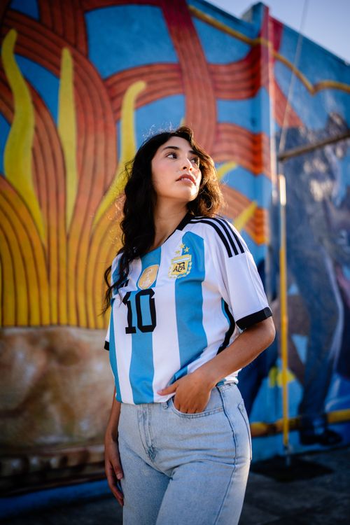 Free Confident young woman in Argentina soccer jersey poses by vibrant mural. Urban and sporty vibe. Stock Photo