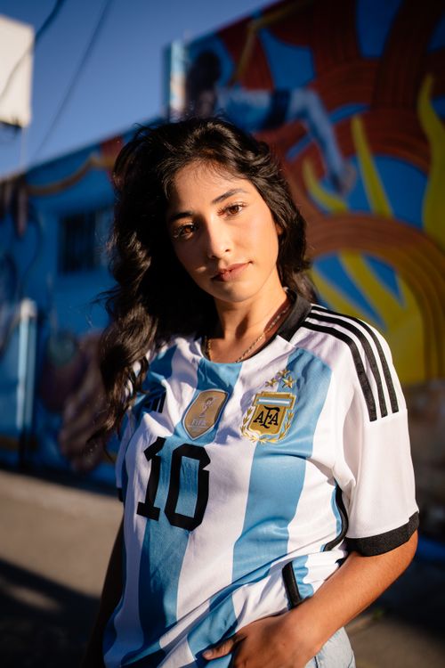 Free Portrait of a woman wearing an Argentina soccer jersey standing in front of a vibrant graffiti wall. Stock Photo
