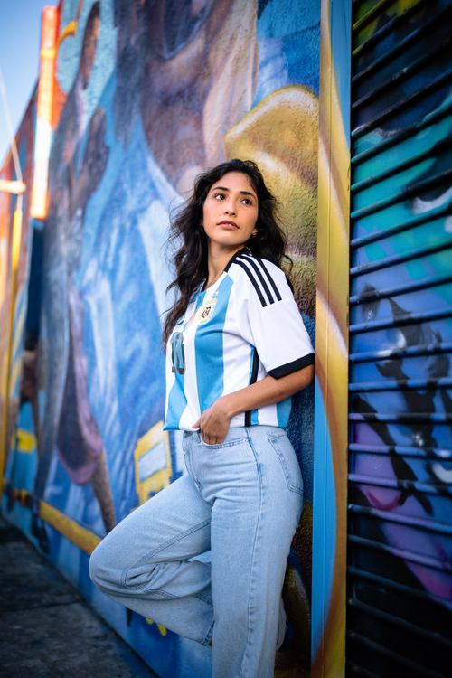 Free A young woman poses against a colorful urban mural wearing an Argentina soccer jersey Stock Photo