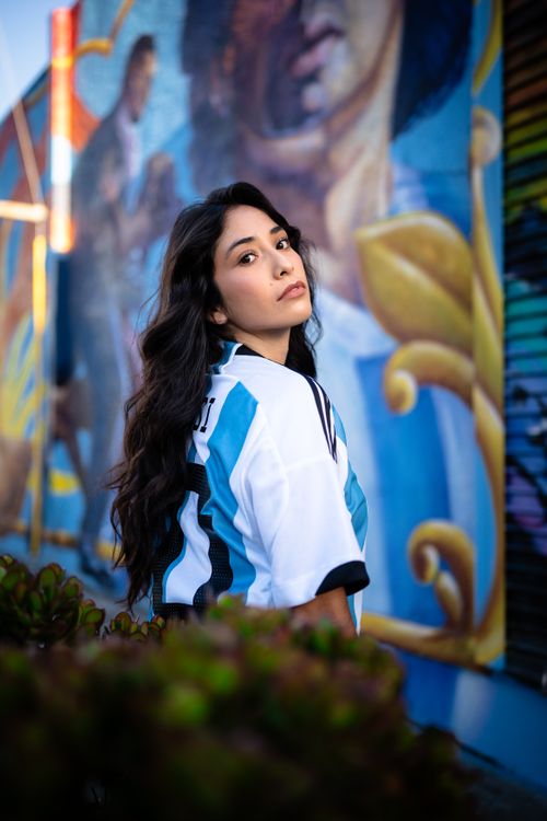 Free Portrait of a woman in football jersey posing beside a colorful mural outdoors. Stock Photo