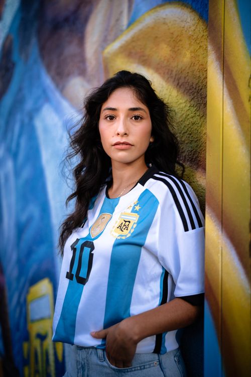Free Portrait of a young woman wearing an Argentina jersey against a colorful mural background. Stock Photo