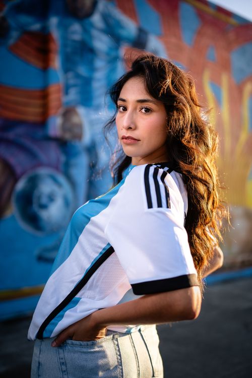 Free A woman poses confidently in front of a colorful urban graffiti wall, wearing a casual sports jersey and jeans. Stock Photo