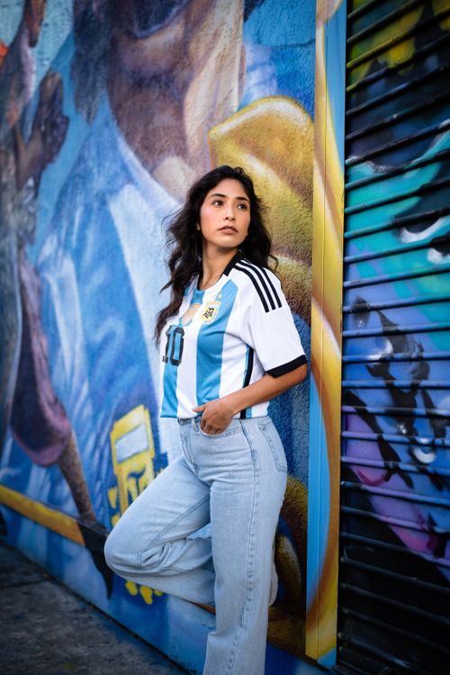 Free Young woman in football jersey leans against a vibrant mural wall outdoors. Stock Photo