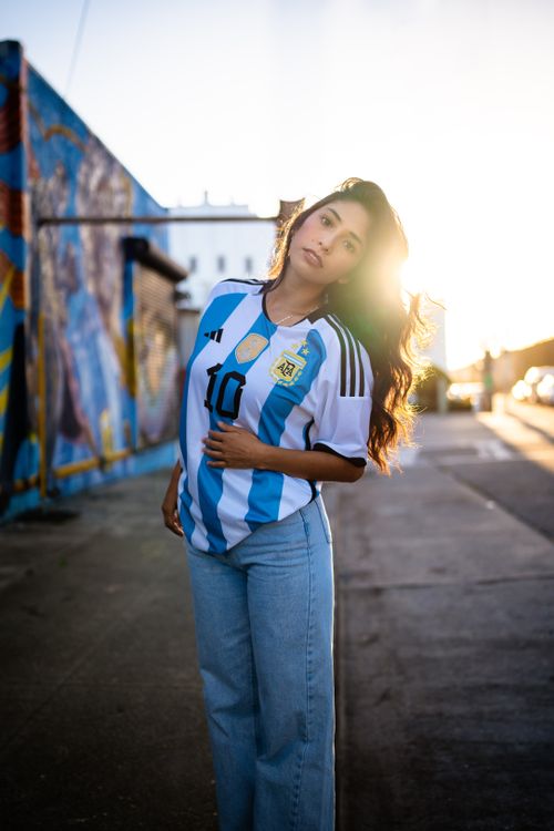 Free Young woman posing in Argentina soccer jersey against urban mural backdrop at sunset. Stock Photo