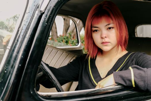 Portrait of a young woman with red hair driving a vintage car, showcasing retro style and vintage vibes.