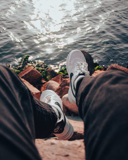 Man in Sneakers Sitting on Rocks near Water