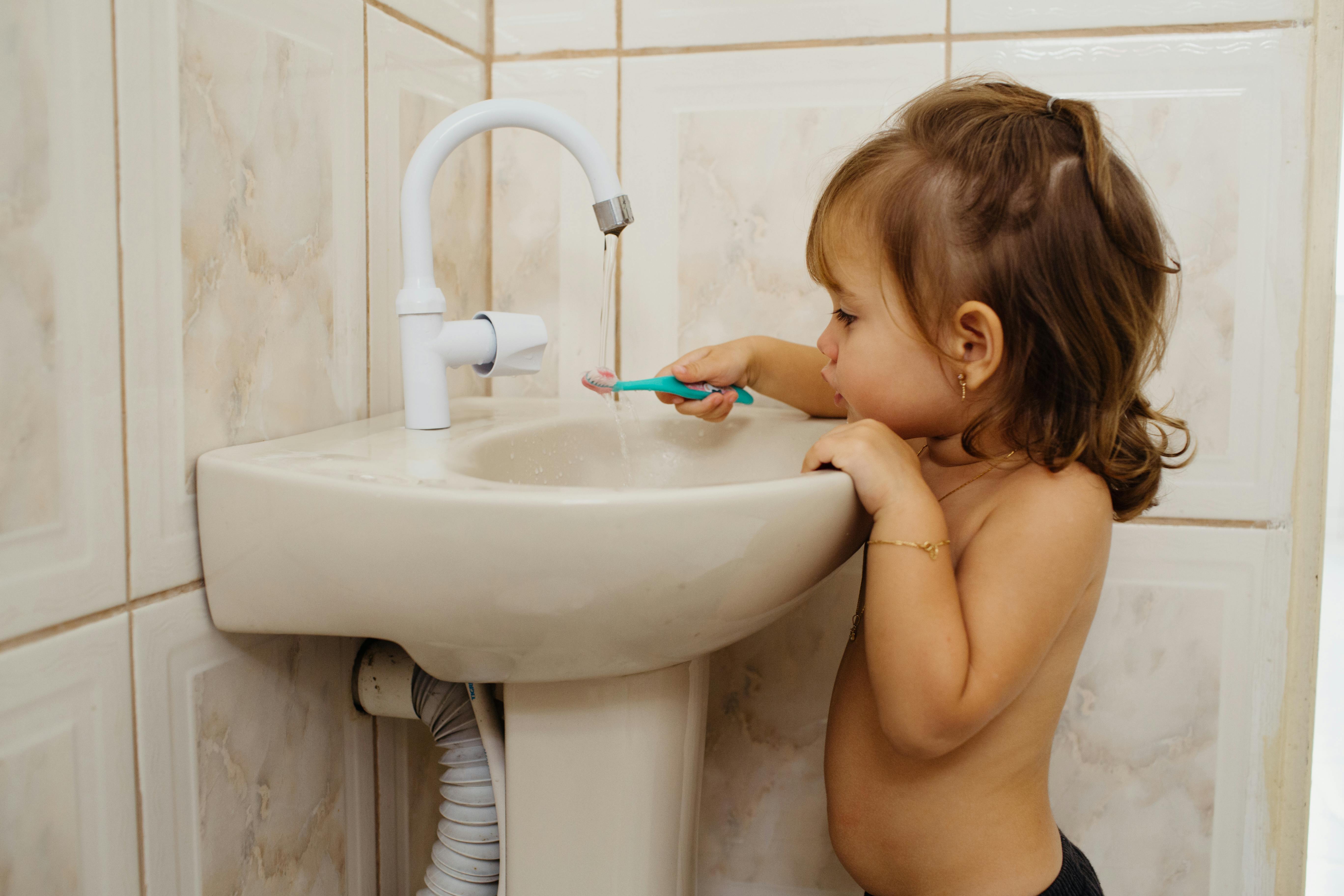 A young child with brown hair brushes teeth using a toothbrush by the sink, showcasing daily hygiene habits.