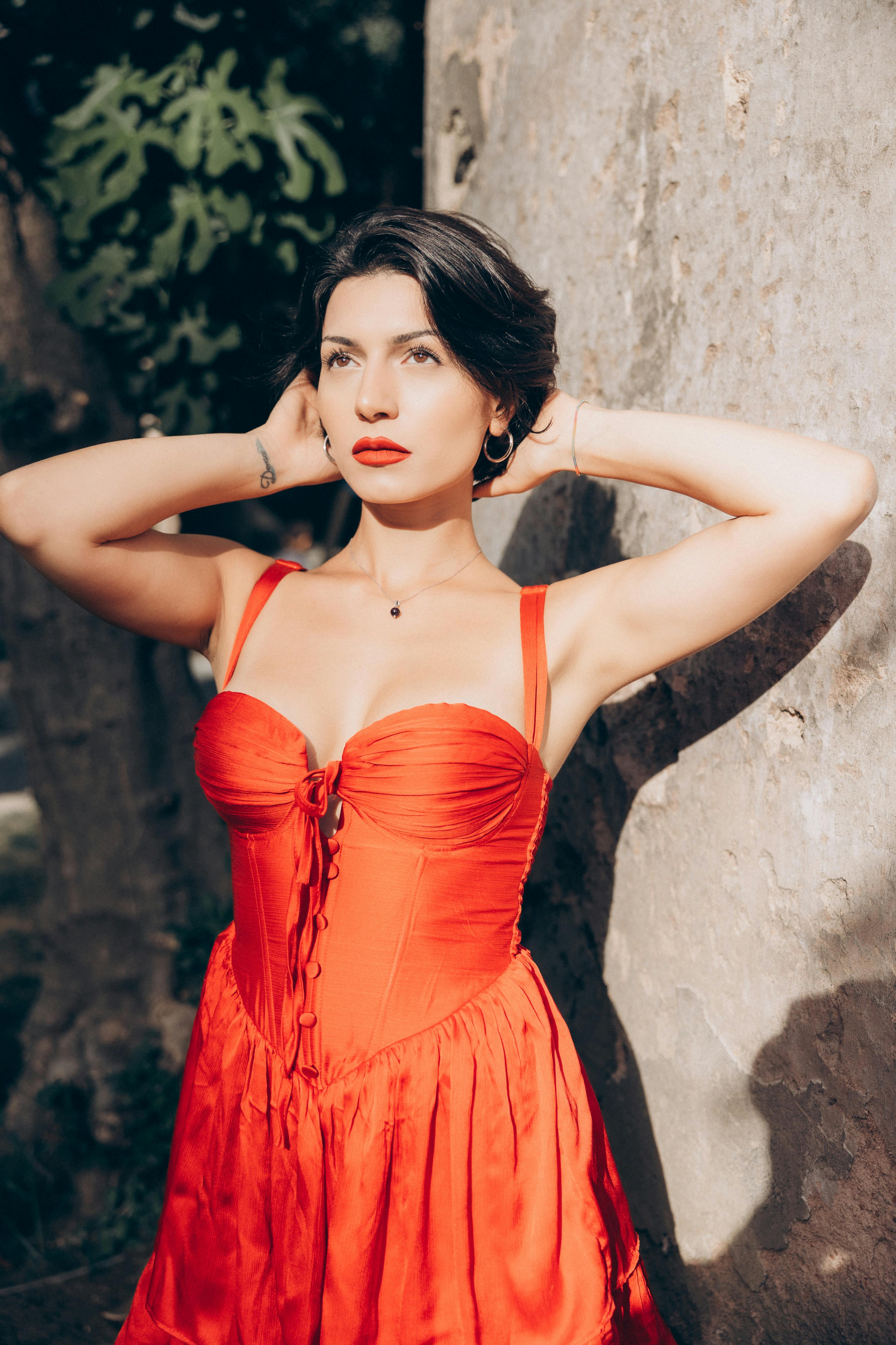 a woman in a red dress posing near a tree