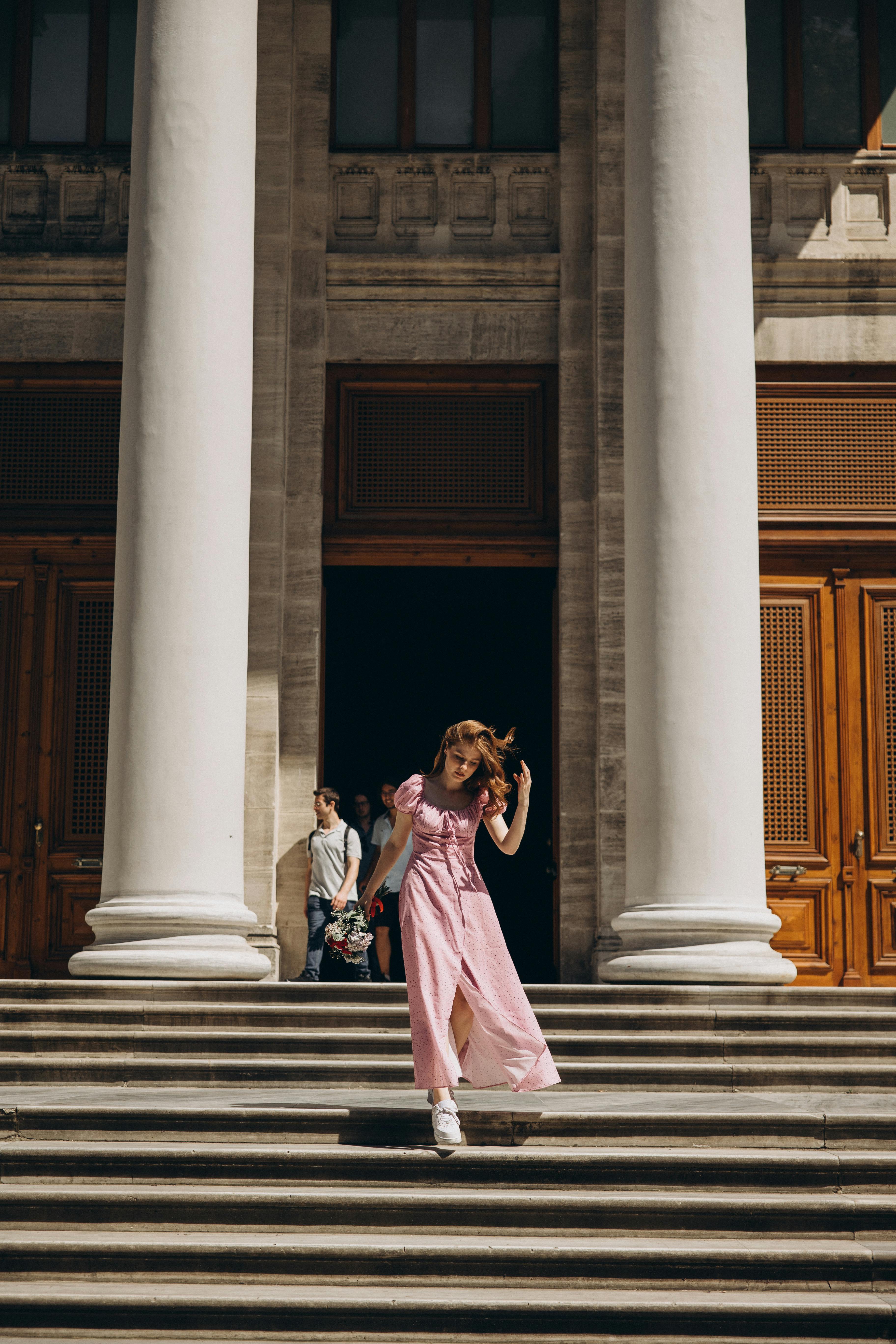 a woman in a pink dress is walking down the steps