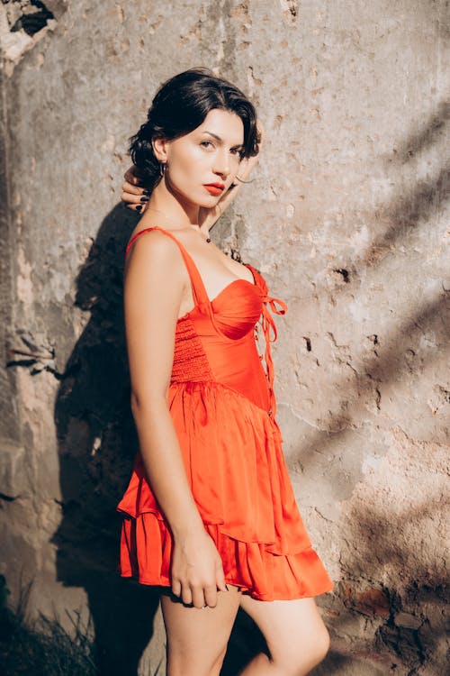 A woman in a red dress posing by a wall