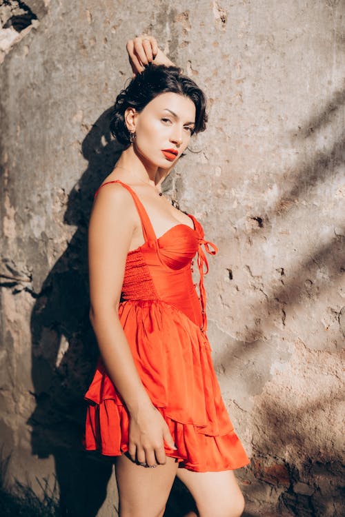 A woman in a red dress posing near a wall