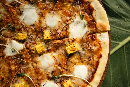 Free Close-up of a mouthwatering paneer pizza with fresh microgreens on a leaf background. Stock Photo