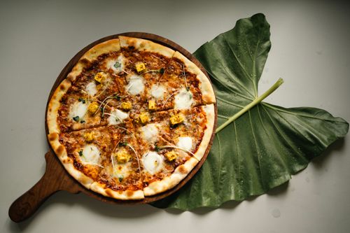 Free Sliced pizza on a wooden tray with a large green leaf on a tabletop. Stock Photo