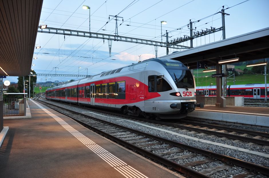 Travelers using free Wi-Fi at a modern SBB train station in Switzerland.