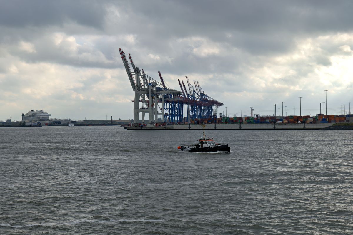 Busy industrial harbor with cranes and vessels under cloudy skies