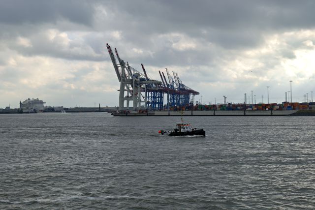 Busy industrial harbor with cranes and vessels under cloudy skies