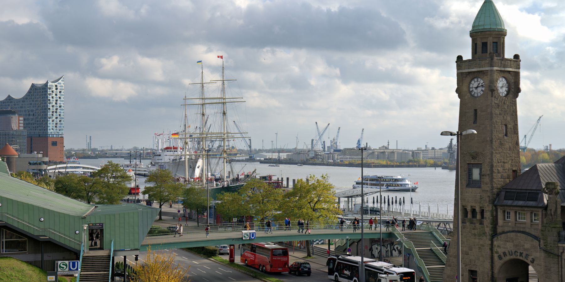 A busy day at Hamburg's harbor featuring the Elbphilharmonie, historic ships, and clock tower.