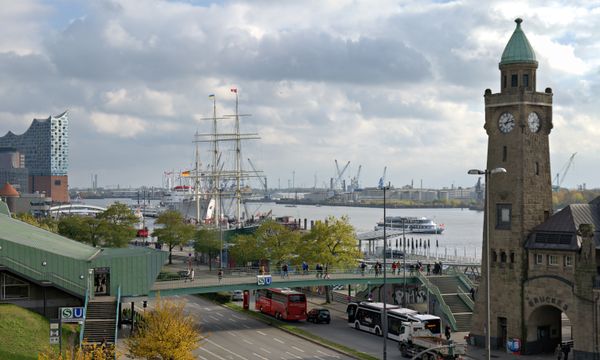 A busy day at Hamburg's harbor featuring the Elbphilharmonie, historic ships, and clock tower.