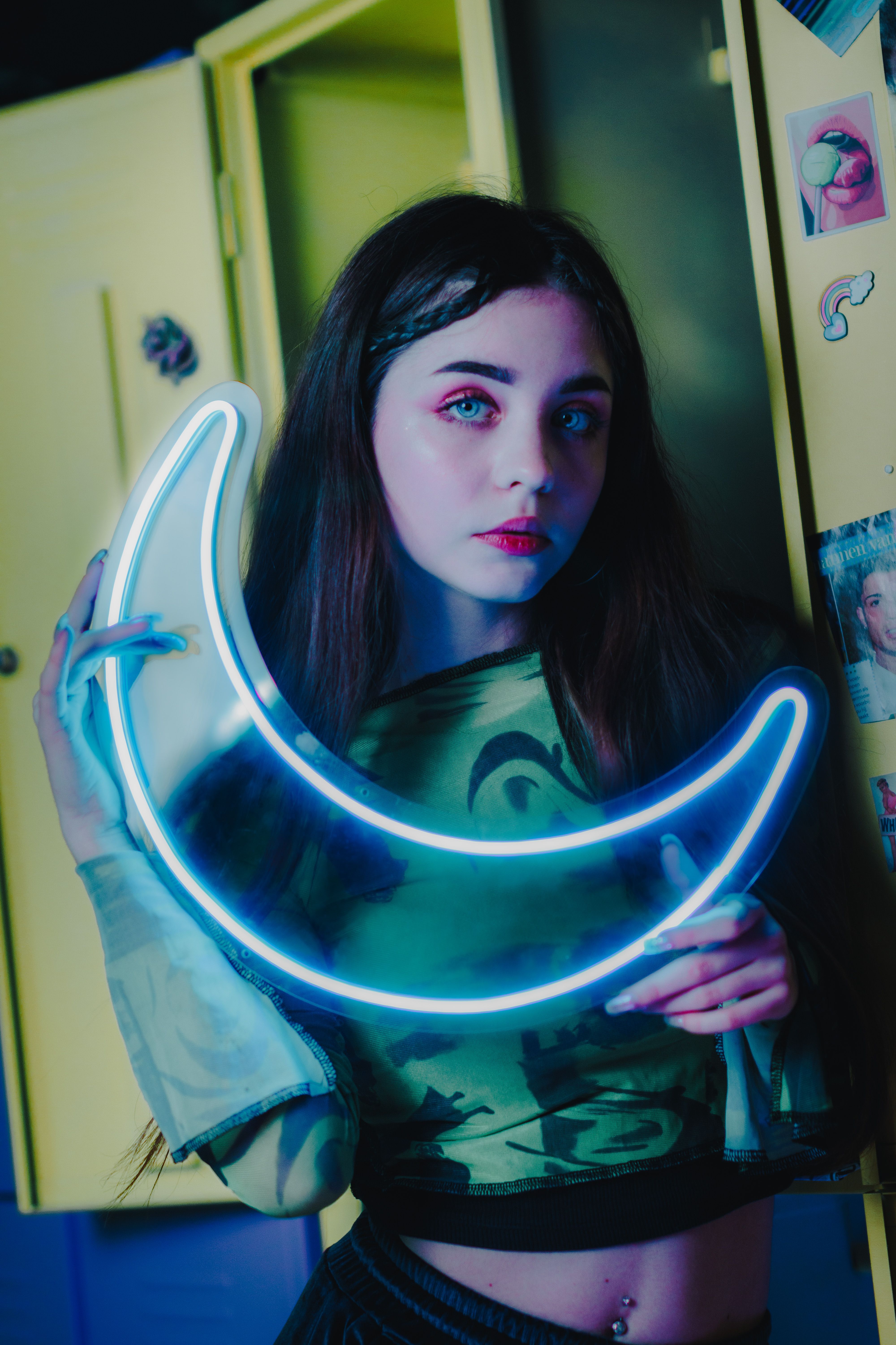 Portrait of a young woman holding a neon crescent moon indoors, capturing a vibrant and moody ambiance.