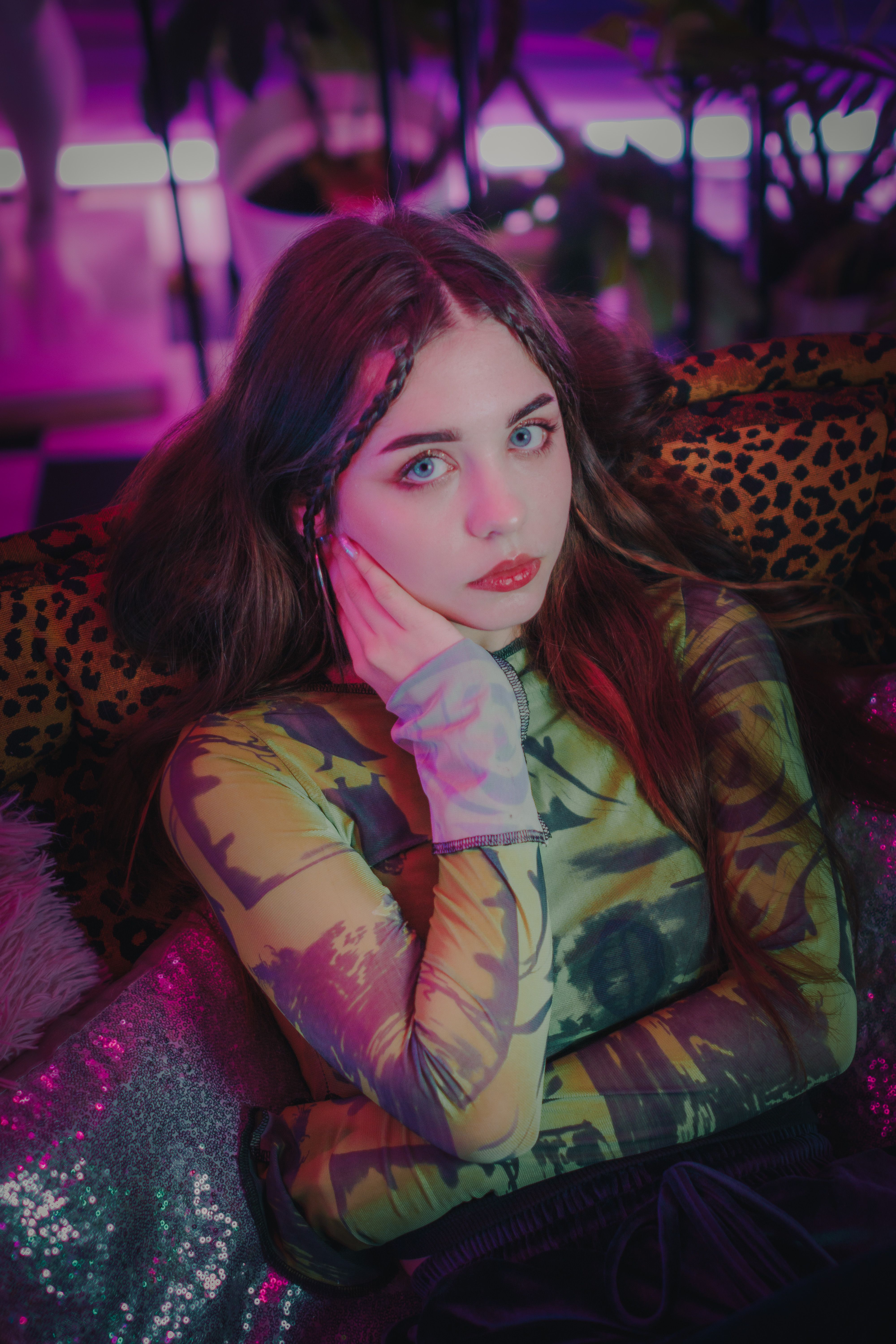 Stylish woman sitting on a leopard print sofa in vibrant neon lighting.