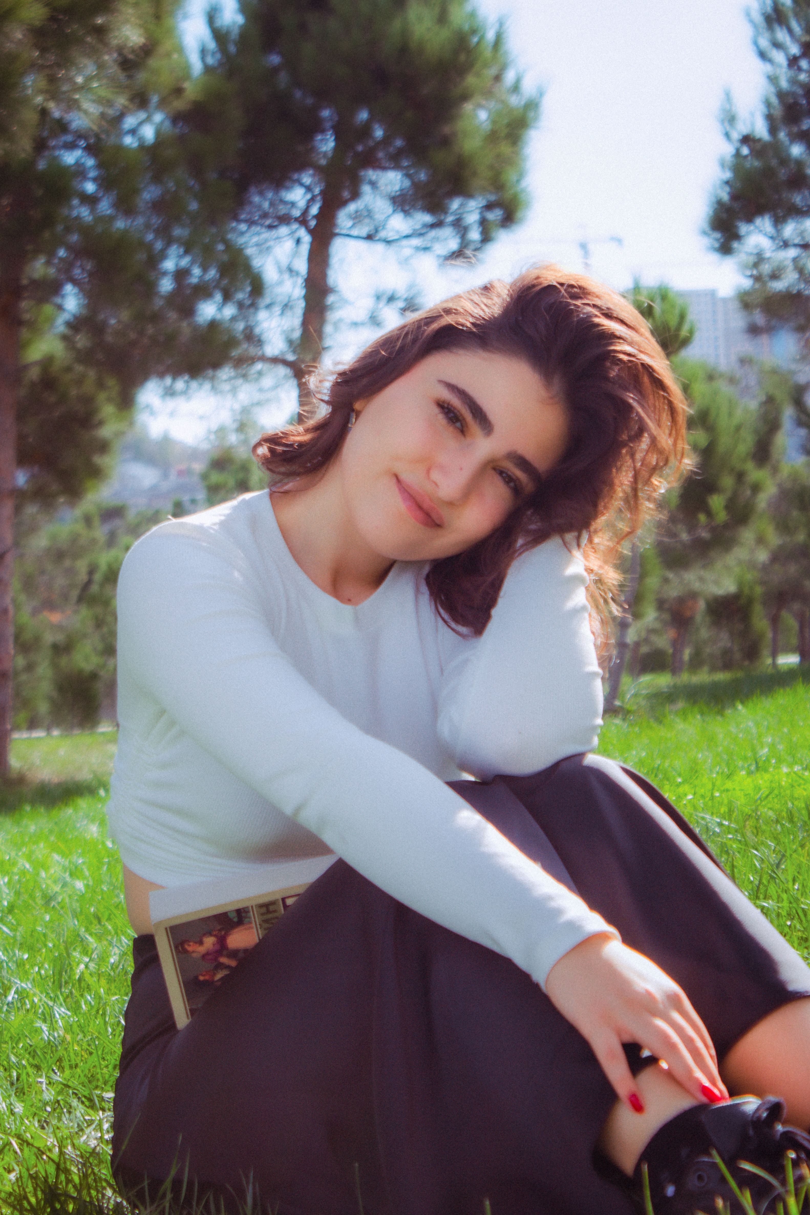 A young woman sits on the green grass in a park, enjoying a sunny day.