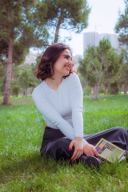 Smiling Young Woman with a Book Sitting on the Grass in the Park